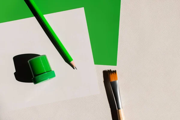 Top view of paintbrush, pencil and jar with paint near white and green papers on textured background — Stock Photo