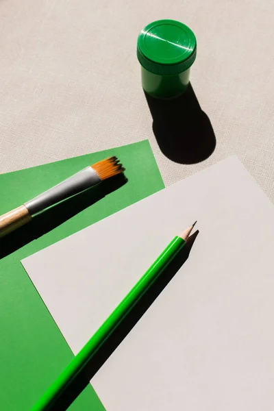 Top view of paintbrush and pencil on white and green papers on textured background — стоковое фото