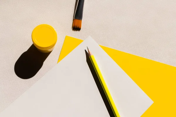 Vue du dessus du pinceau, du crayon et du pot avec de la peinture près des papiers blancs et jaunes sur fond texturé — Photo de stock