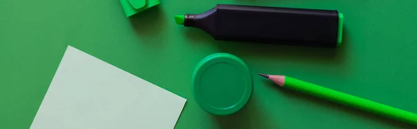Vista superior del lápiz, crayón, tarro con pintura y rotulador cerca de la nota de papel en verde, pancarta - foto de stock