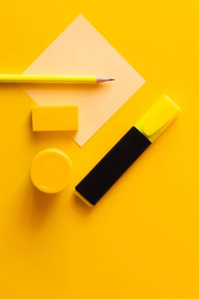 Вид зверху на гумку, олівець, баночку з фарбою та маркерну ручку біля паперової ноти на жовтому — стокове фото