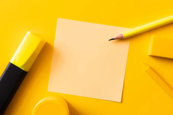 Vista superior de artigos de papelaria perto da nota de papel em branco no amarelo — Fotografia de Stock