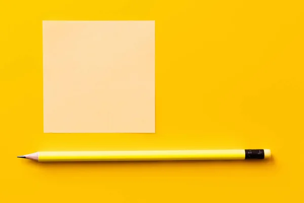 Top view of sharp pencil near blank paper note on yellow — стоковое фото