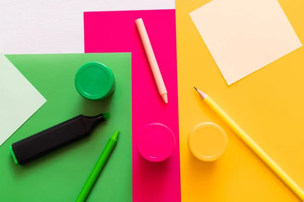Top view of stationery near jars with paint on colorful background — Stock Photo
