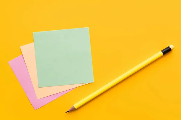 Top view of pencil near multicolored paper notes on yellow background — стоковое фото