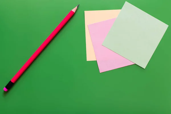 Vista superior do lápis perto de notas de papel multicoloridas no fundo verde — Fotografia de Stock