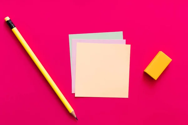 Вид зверху на олівець і гумку біля різнокольорових паперових нот на рожевому фоні — стокове фото