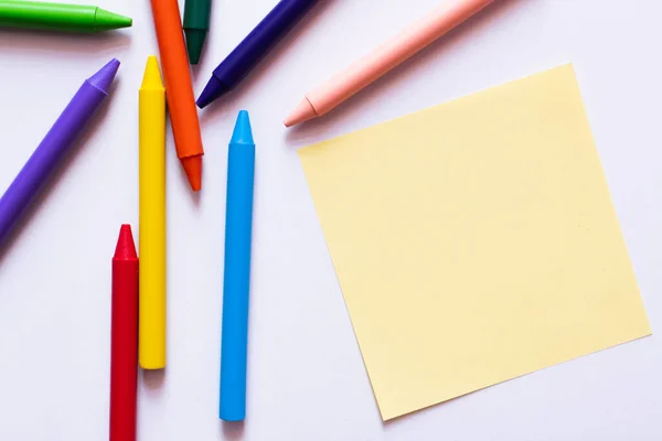 Top view of colorful crayons near yellow paper note on white — Stock Photo