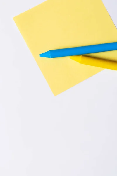 Top view of blue and yellow crayons on paper note isolated on white — стоковое фото