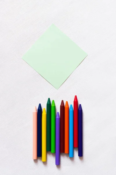 Top view of colorful crayons near empty paper note on textured white background — Stock Photo