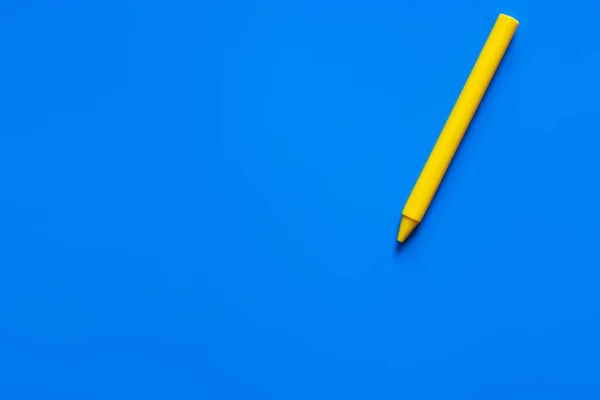 Top view of yellow crayon on blue background — стоковое фото