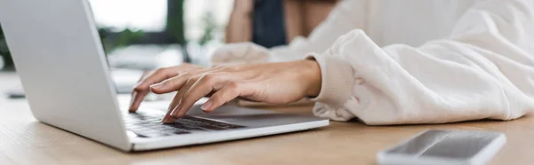 Cropped view of businesswoman using laptop near blurred smartphone in office, banner — Foto stock