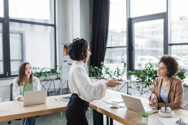 Muslim businesswoman talking to african american colleague near papers and devices in office — Stock Photo