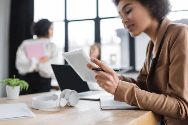 Donna d'affari afroamericana offuscata che utilizza tablet digitale vicino a notebook e cuffie in ufficio — Foto stock