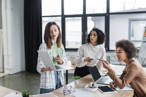 Empresárias multiculturais apontando para laptop enquanto trabalham no escritório — Fotografia de Stock