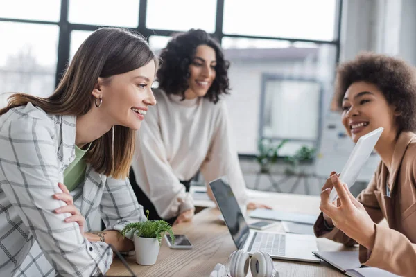 Fröhliche interrassische Geschäftsfrauen blicken in der Nähe einer afrikanisch-amerikanischen Amtskollegin auf ein digitales Tablet — Stockfoto