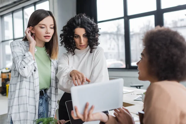 Interracial businesswomen looking at blurred digital tablet near african american colleague in office — Stockfoto