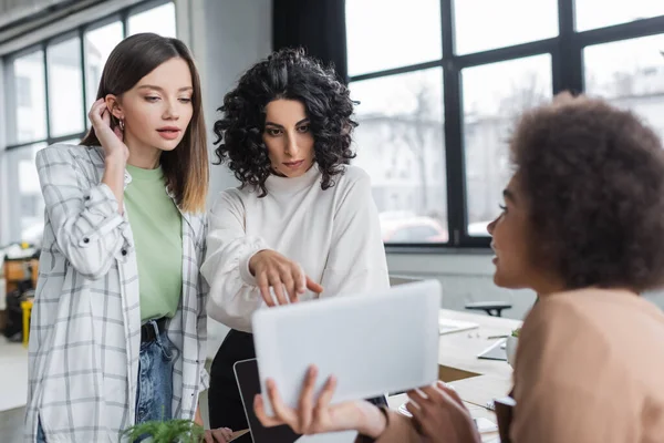 Interracial businesswomen looking at blurred digital tablet near african american colleague in office — Photo de stock