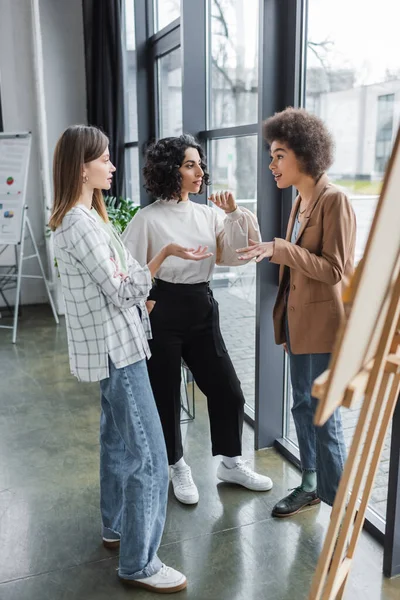 Imprenditrici multiculturali che parlano vicino al tabellone offuscato in ufficio — Foto stock