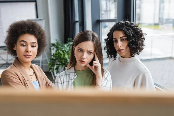 Pensive businesswoman looking at blurred board near multiethnic colleagues — Foto stock