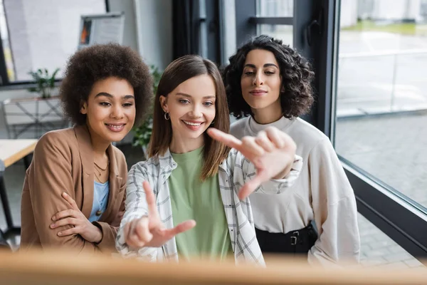 Cheerful interracial businesswomen looking at blurred board in office — Stockfoto