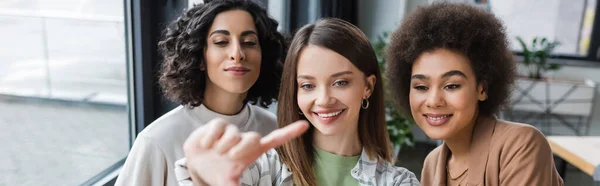 Lächelnde Geschäftsfrau zeigt mit dem Finger auf multikulturelle Kollegen im Büro, Transparent — Stockfoto