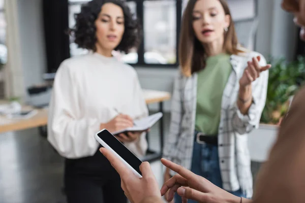 African american businesswoman pointing at cellphone near blurred multiethnic colleagues in office — стокове фото