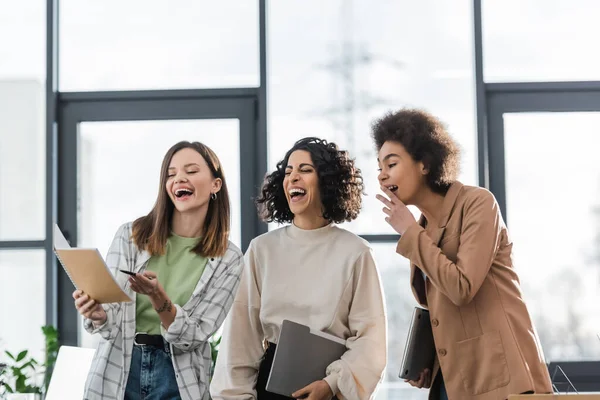 Femmes d'affaires interraciales excitées regardant un cahier au bureau — Photo de stock