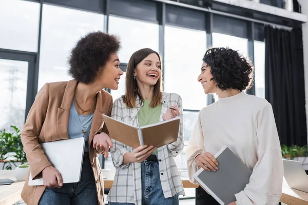 Fröhliche multiethnische Geschäftsfrauen, die im Büro mit Laptop und Papieren arbeiten — Stockfoto