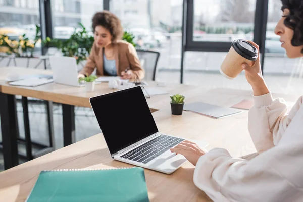 Arabian businesswoman using laptop and holding coffee to go in office — стоковое фото