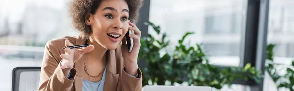 Fröhliche afrikanisch-amerikanische Geschäftsfrau telefoniert und hält Stift im Büro, Banner — Stockfoto