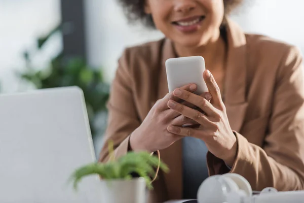 Vue recadrée d'une femme d'affaires afro-américaine floue utilisant un téléphone portable au bureau — Photo de stock