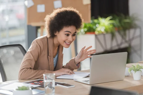 Femme d'affaires afro-américaine positive ayant un appel vidéo sur un ordinateur portable au bureau — Photo de stock