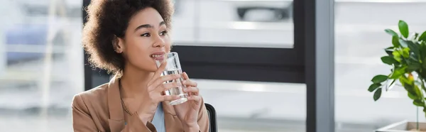 Femme d'affaires afro-américaine positive tenant un verre d'eau au bureau, bannière — Photo de stock