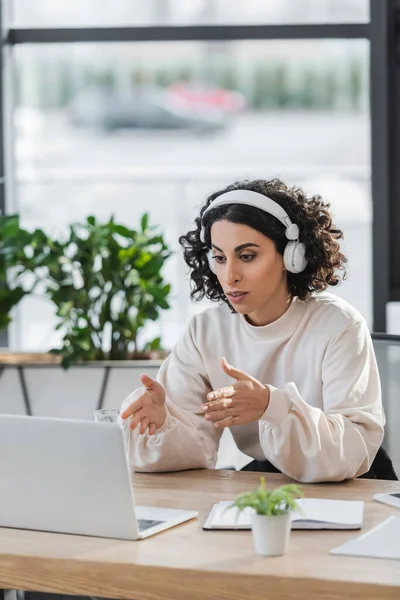Arabe femme d'affaires dans les écouteurs ayant appel vidéo sur ordinateur portable dans le bureau — Photo de stock