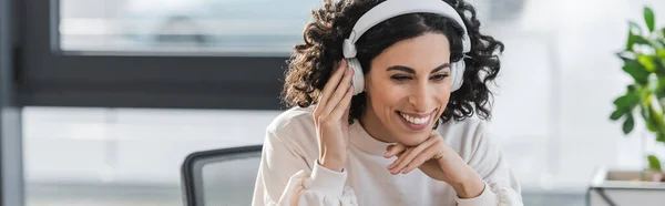 Feliz mulher de negócios muçulmana ouvindo música em fones de ouvido no escritório, banner — Fotografia de Stock