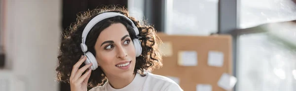 Щаслива арабська комерсантка, яка користується навушниками в офісі, банер. — стокове фото