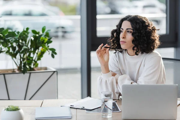 Arabian businesswoman holding pen near laptop and clipboard in office — стоковое фото