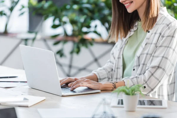 Vue recadrée d'une femme d'affaires souriante utilisant un ordinateur portable près d'appareils au bureau — Photo de stock