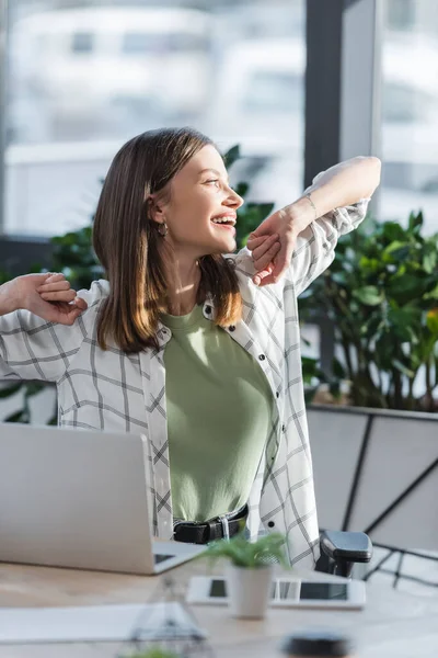 Glückliche junge Geschäftsfrau, die in der Nähe von Gadgets im Büro wegschaut — Stockfoto