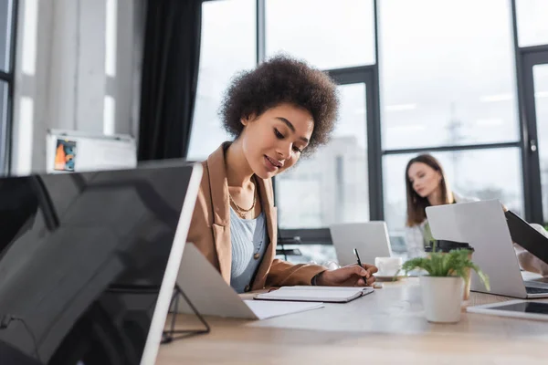 Lächelnde afrikanisch-amerikanische Geschäftsfrau blickt im Büro auf Notizbuch — Stockfoto