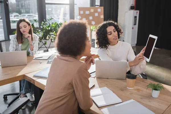 Empresaria musulmana señalando tableta digital cerca de colegas y documentos sobre la mesa - foto de stock