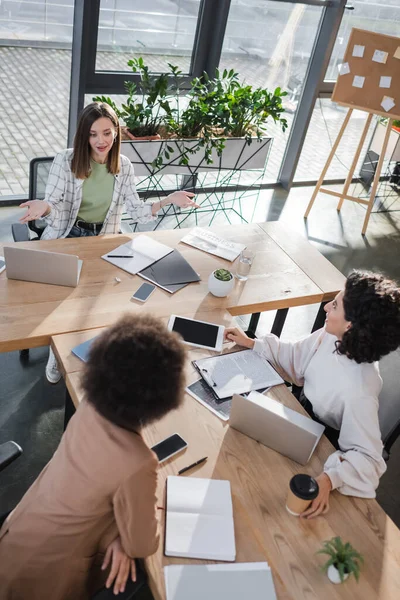 Vista aérea de mujeres de negocios interracial que trabajan cerca de documentos y dispositivos en la oficina - foto de stock