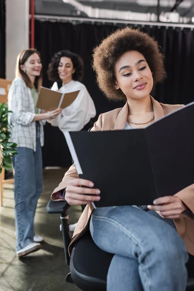 Cheerful african american businesswoman looking at paper folder near blurred interracial colleagues in office — Photo de stock