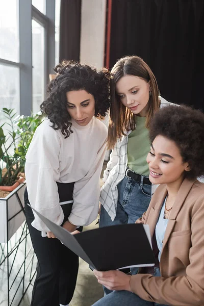 Multicultural businesswomen looking digital tablet looking at paper folder in office — стоковое фото