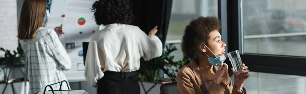 African american businesswoman in medical mask holding water in office, banner — Stock Photo