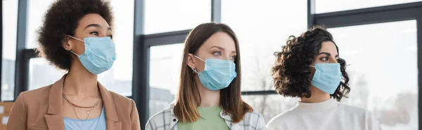 Imprenditrici multiculturali mascherate mediche che distolgono lo sguardo in ufficio, striscione — Foto stock