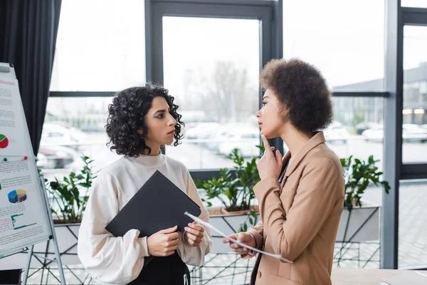 Pensive interracial businesswomen holding newspaper and paper folder in office — Foto stock