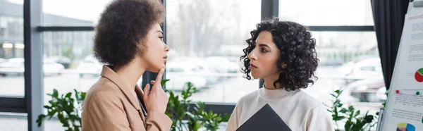 Pensativa mujer de negocios afroamericana mirando el rotafolio cerca de colega musulmán en la oficina, pancarta — Stock Photo