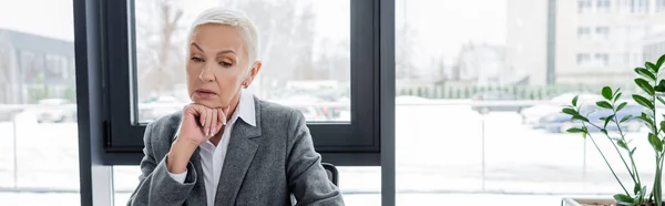 Senior economist with grey hair holding hand near chin while thinking in office, banner - foto de stock